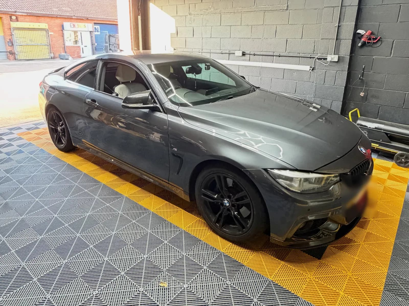 A dark grey BMW F32 420i in the CODEMYBM workshop bay, on yellow and grey floor tiles